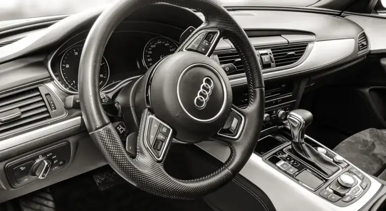 Close-up of an Audi car interior featuring the steering wheel and center console in black and white.