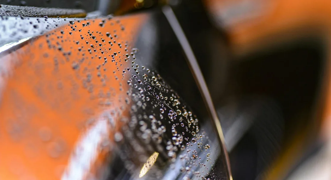 Close-up of a glossy orange car panel with numerous water droplets on the surface