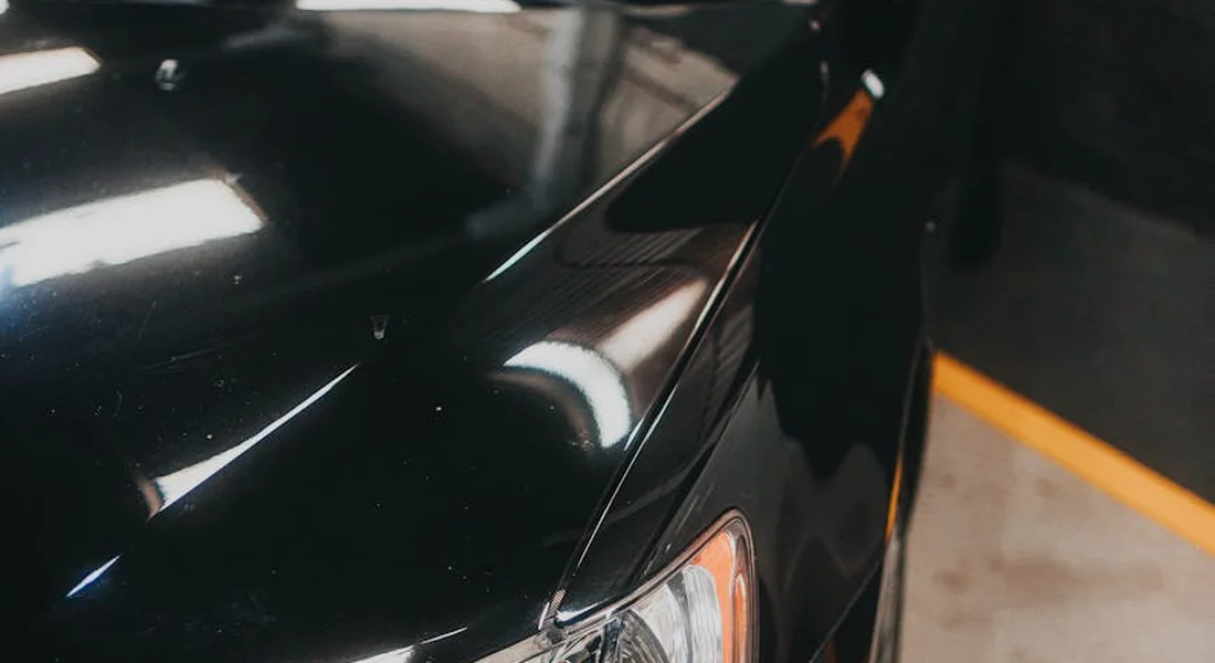Close-up of a glossy black car body with reflections of overhead lights in a parking garage.