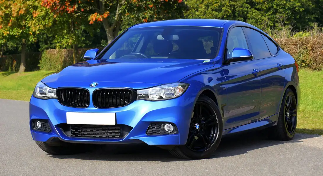 Front-left view of a bright blue BMW sedan parked on a driveway with green trees in the background.