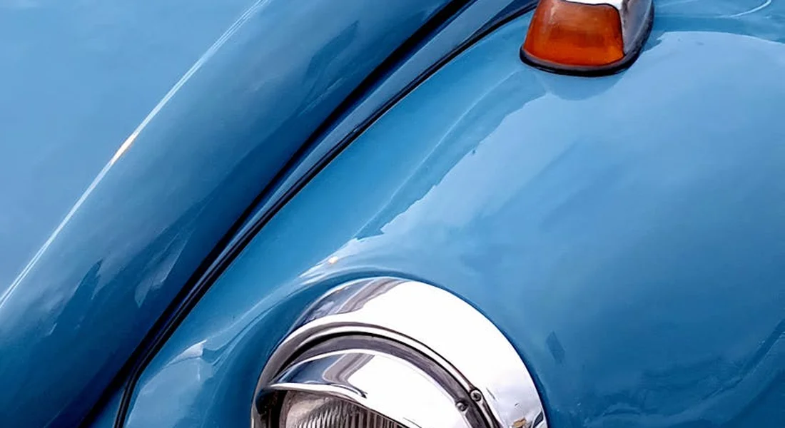 Close-up of a blue car's front fender with a round headlight and an orange indicator light