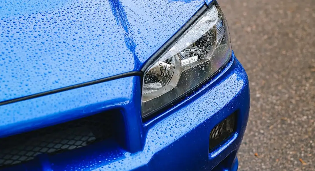 Close-up of a blue car's front end with water droplets on the paint near the headlight