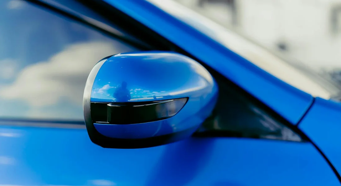 Close-up of a blue car's side mirror and window, illustrating prep work before cleaning the windows for a streak-free finish.