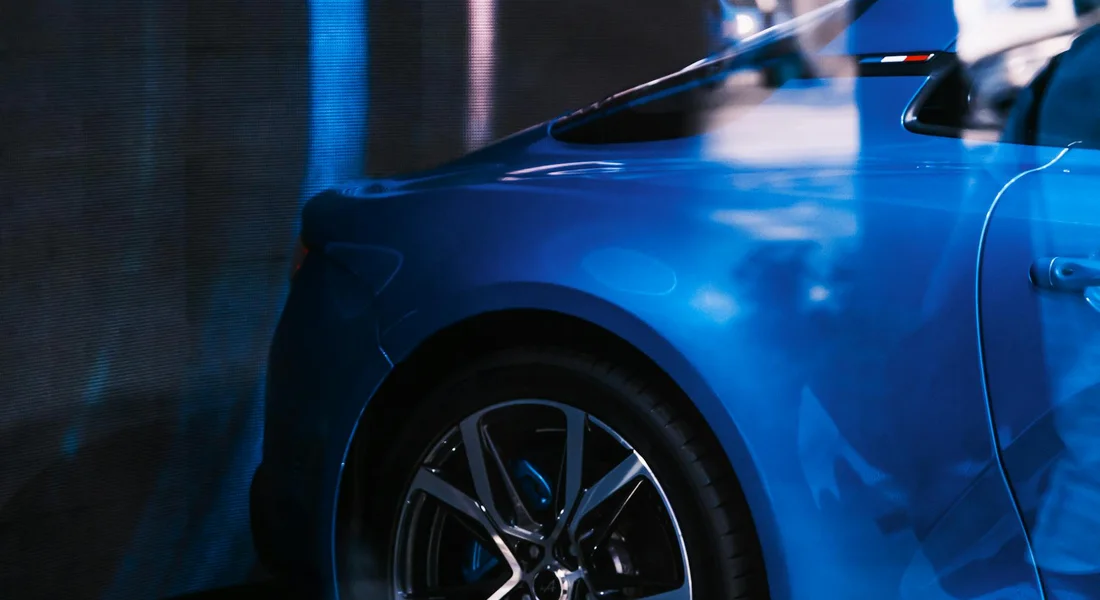 Close-up of a glossy blue car showing the front wheel and fender under blue-tinted lighting