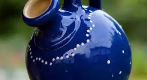 Close-up of a glossy blue ceramic jug with a curved spout and dotted white pattern