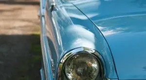 Close-up of a blue vintage car highlighting a rounded headlight and glossy body.