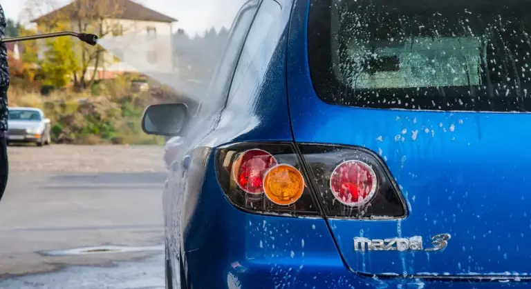 Rear view of a blue Mazda3 with water droplets on the rear window, parked outdoors.