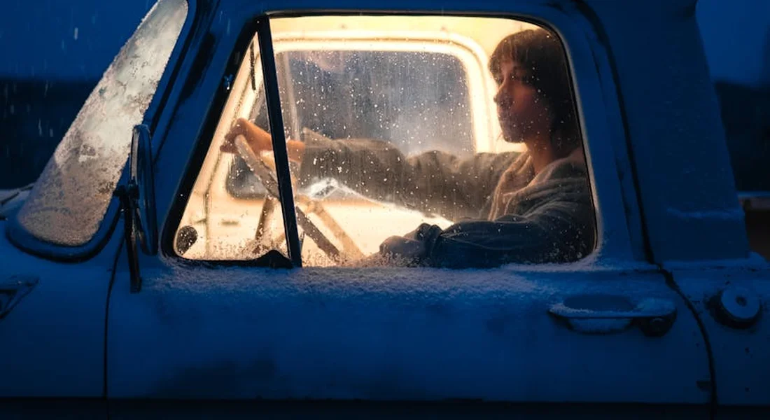 Driver seated in the blue truck, seen through the side window with condensation on the glass.
