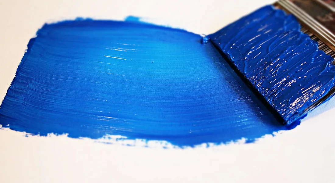 Close-up of a vivid blue paint smear created by a brush on a white surface.