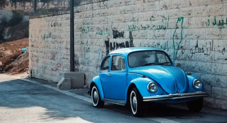 Blue vintage Volkswagen Beetle parked beside a graffiti-covered wall