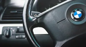 Close-up of a BMW steering wheel inside a car cabin, with the dashboard and controls visible.