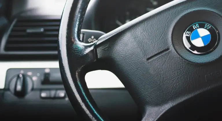 Close-up of a BMW steering wheel inside a car cabin, with the dashboard and controls visible.