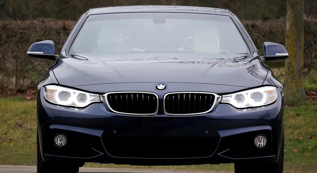 Front view of a dark blue BMW sedan with headlights illuminated