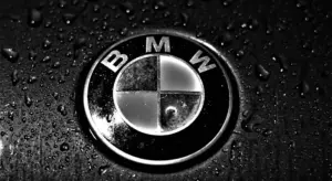 Close-up of BMW roundel on a dark, wet car surface with water droplets.