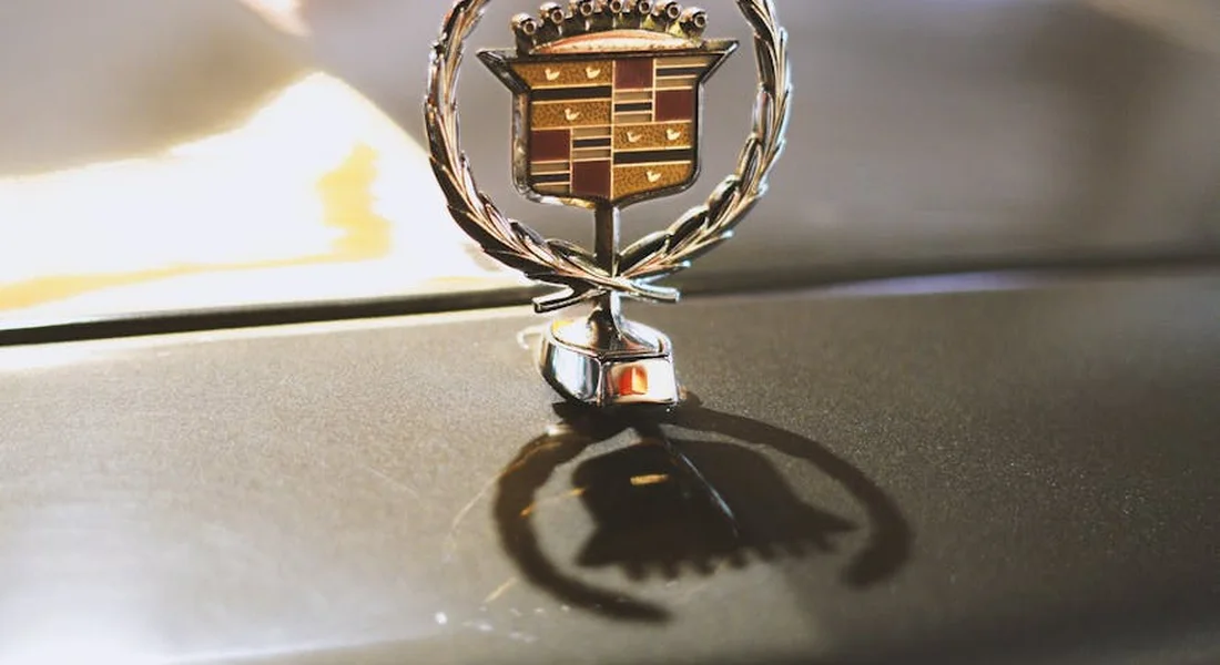 Close-up of a Cadillac hood ornament with its reflection visible on the car's paint.