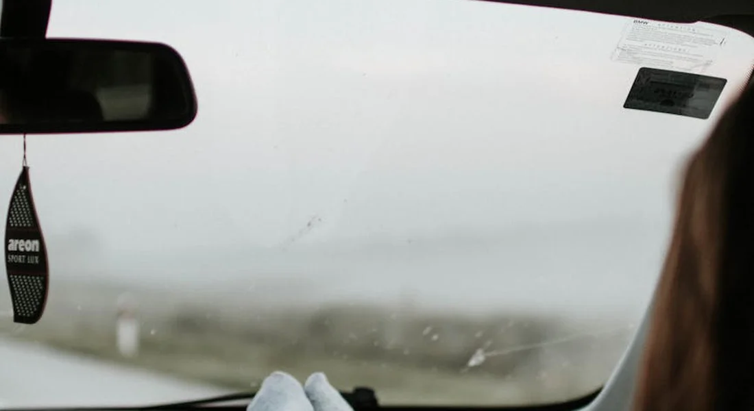 Inside a car, viewed through the windshield, with a small hanging tag from the rearview mirror and blue gloves resting on the dashboard.