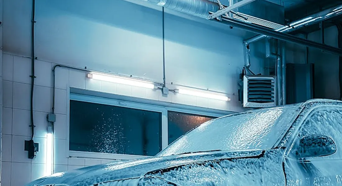 A car being detailed in a professional wash bay with soap foam and blue lighting