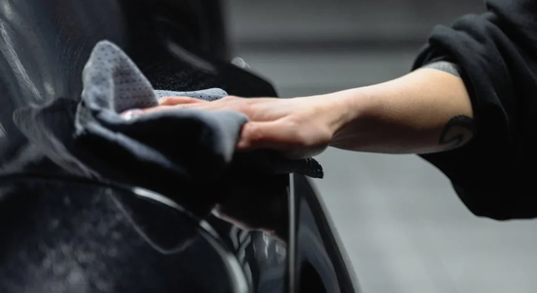 Close-up of a hand polishing a car's glossy surface with a microfiber cloth