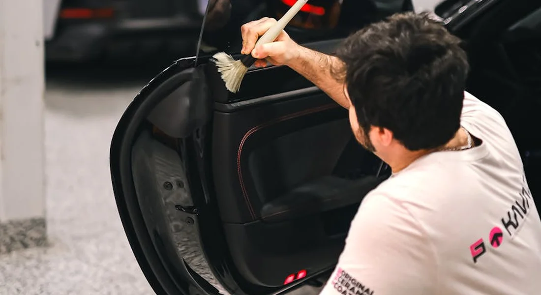 A car detailer brush-cleaning the interior door panel of a vehicle