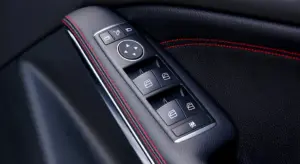 Close-up of a car door panel with window control switches and black leather with red stitching