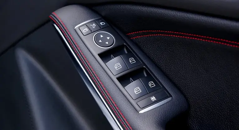 Close-up of a car door panel with window control switches and black leather with red stitching