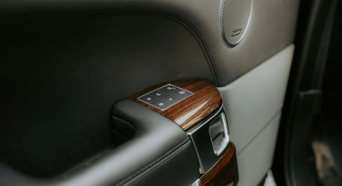 Close-up of a car's interior door panel featuring wood-grain trim and a control panel.