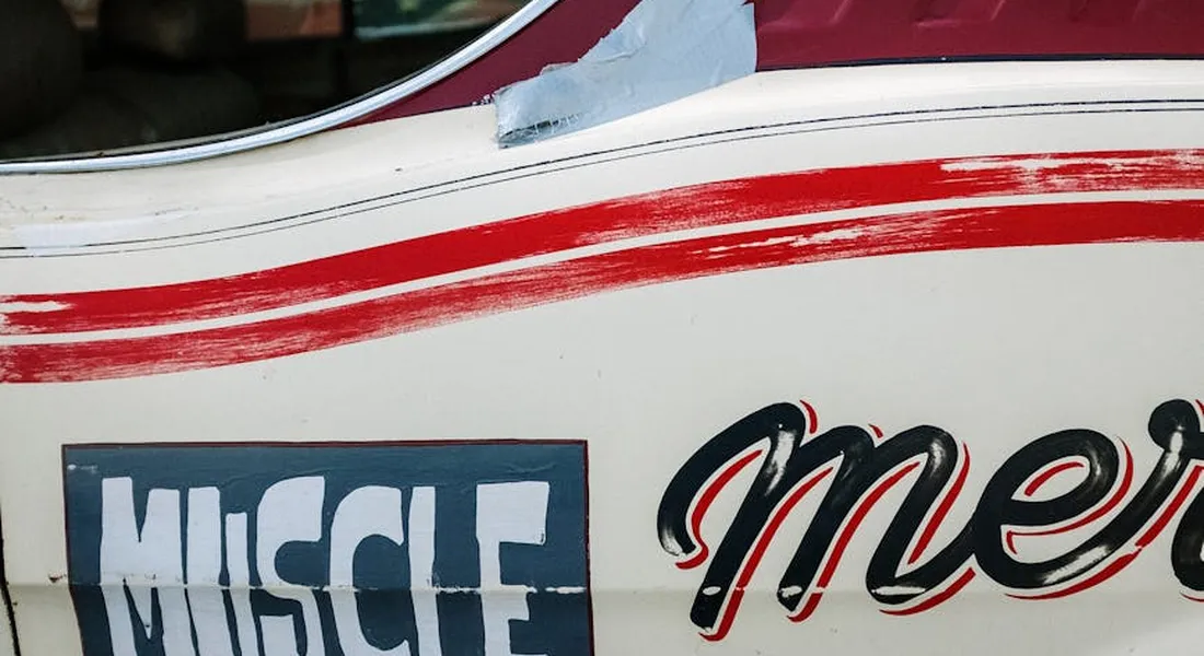 Close-up of a car door with muscle car graphics, featuring a red stripe and bold MUSCLE lettering