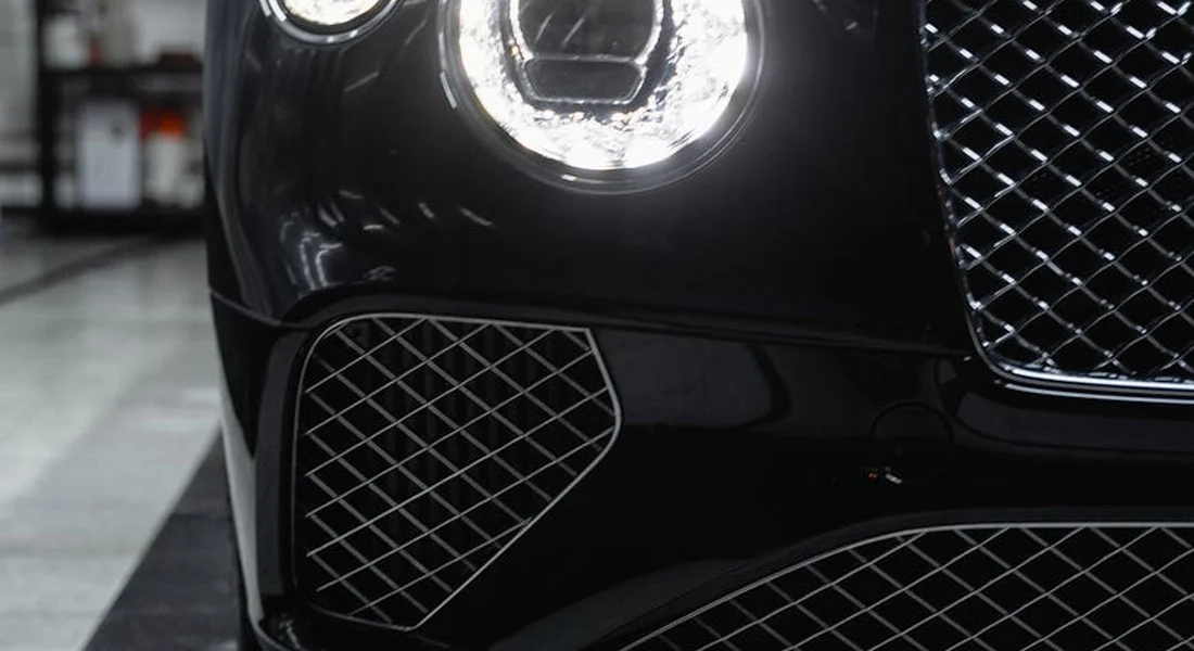 Close-up of a glossy black car headlight and front grille