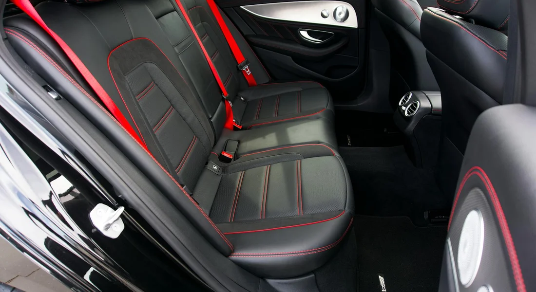 Back seat area of a car with black leather upholstery and red contrast stitching.