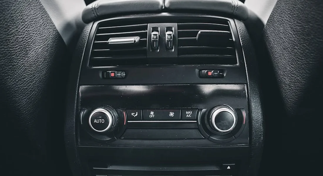 Close-up of a car's climate-control panel and air vents inside a dark interior.