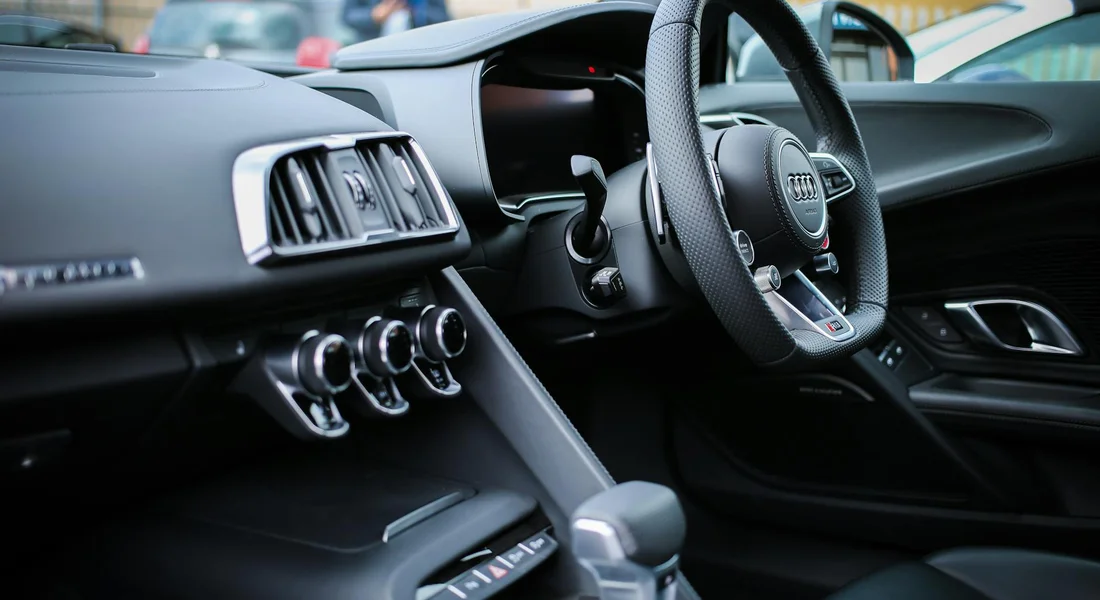 Interior of a modern car showing the dashboard, center console, and steering wheel with control knobs and a leather trim.