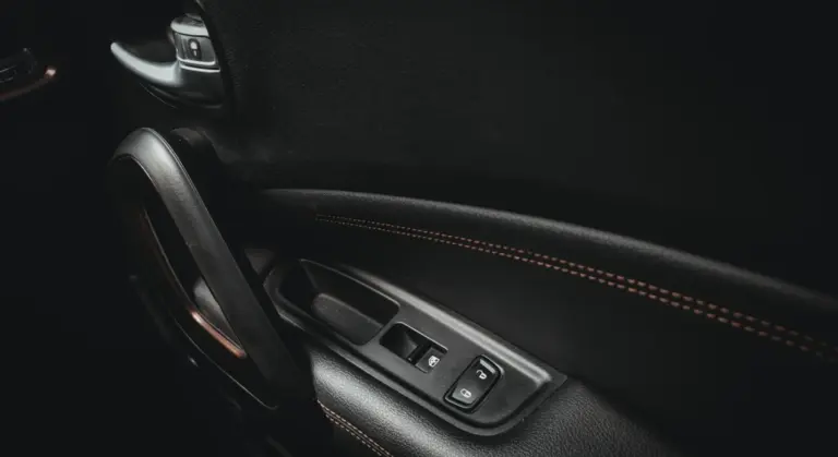 Close-up of a car's interior door panel featuring window controls and stitched leather