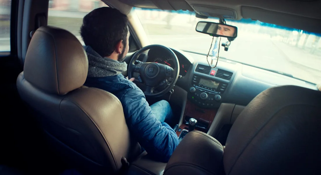 Driver sitting in the front seat of a car with the dashboard and steering wheel in view.