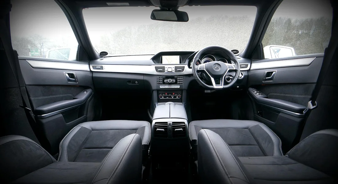 Front interior of a sedan with black leather seats, steering wheel, and center console, photographed from the back seats.