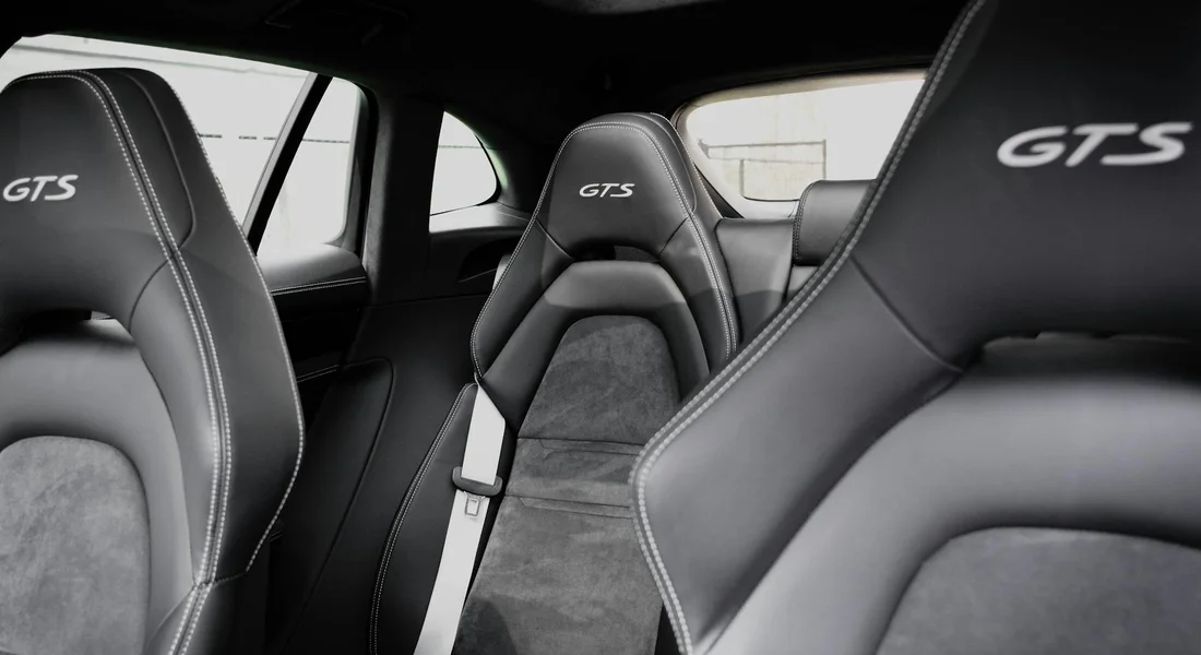 Close-up of a car interior with dark upholstery and white contrast stitching, featuring GTS embroidered headrests.