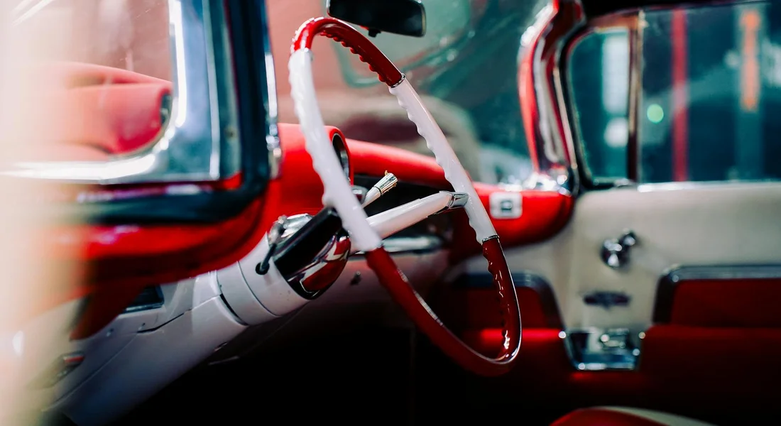 Interior of a vintage red-and-white car showing the steering wheel and dashboard.