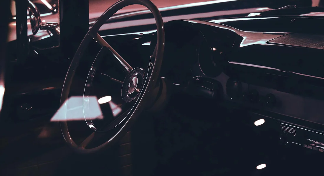 Dim, moody interior of a vintage car showing the steering wheel and dashboard, suggesting hidden moisture and odor sources.