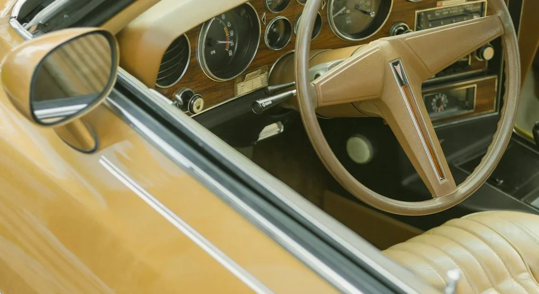 Close-up view of a tan leather car interior, including the steering wheel and dashboard, photographed from the driver's side.