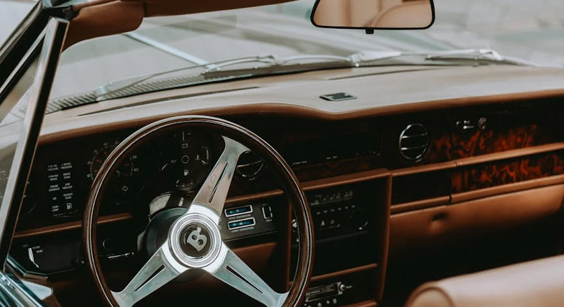 Close-up view of a classic car interior featuring a brown leather dashboard and a metal steering wheel.