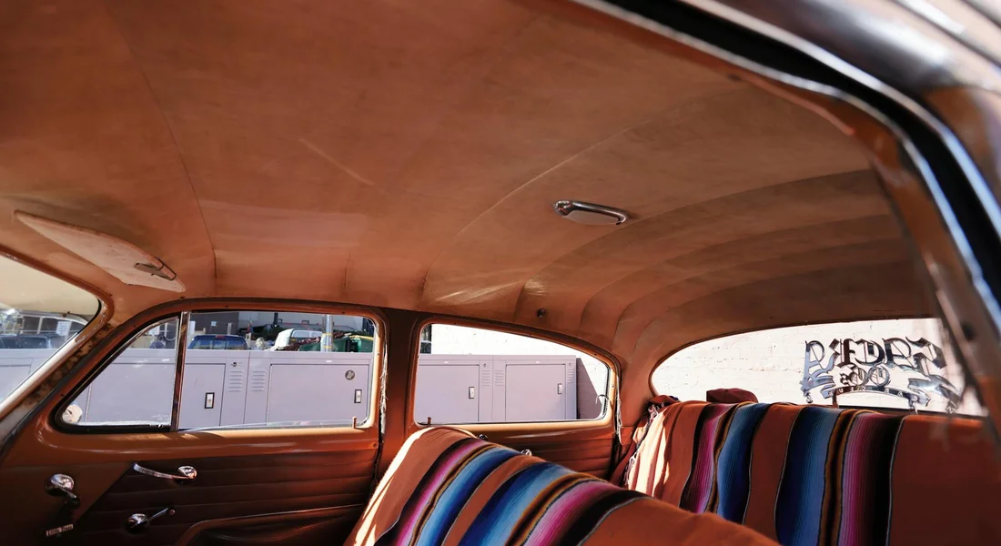 Vintage car interior with tan fabric headliner and doors, featuring colorful striped seat covers.
