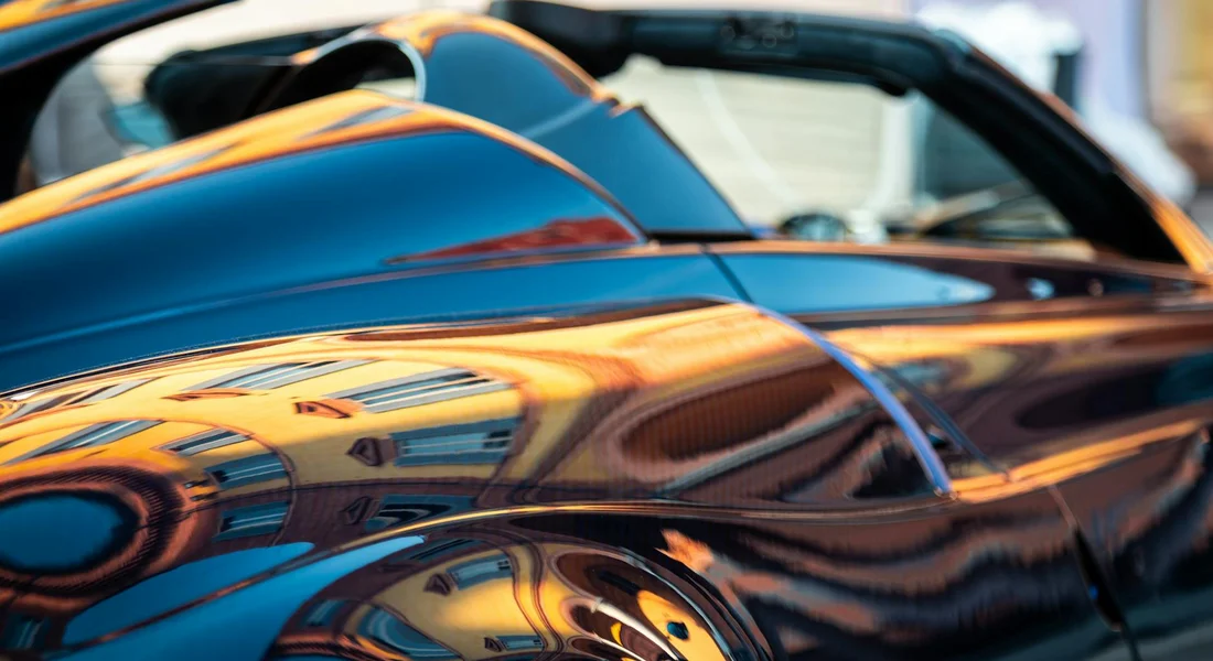 Close-up of a glossy blue car with orange reflections, emphasizing a high-quality paint finish.