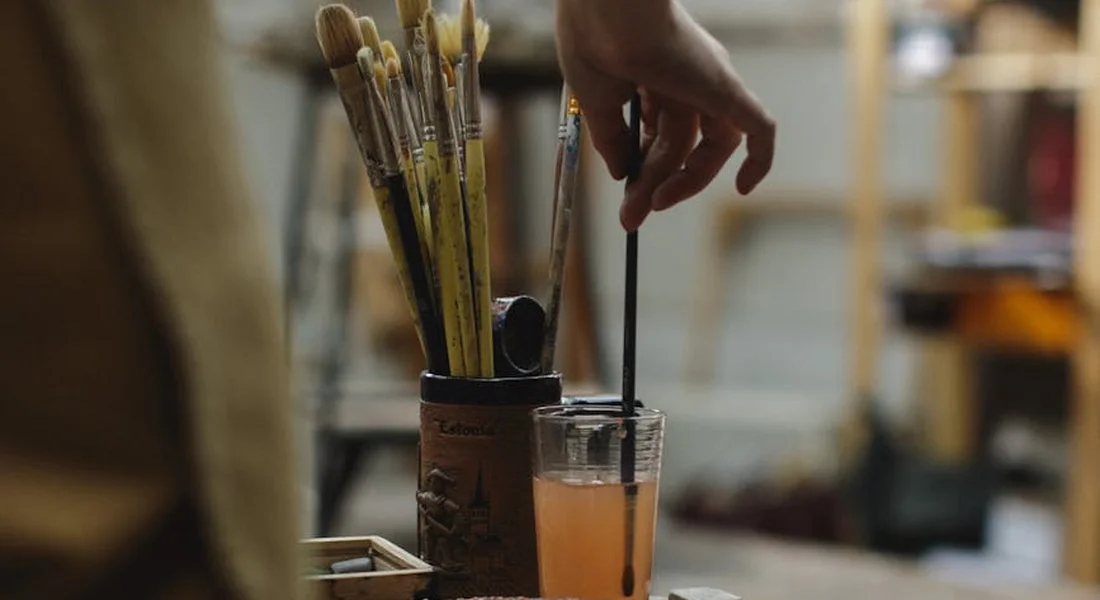 Workshop scene with paintbrushes in a jar and a hand reaching for a tool, illustrating the preparation steps in finding a car's exact paint color.