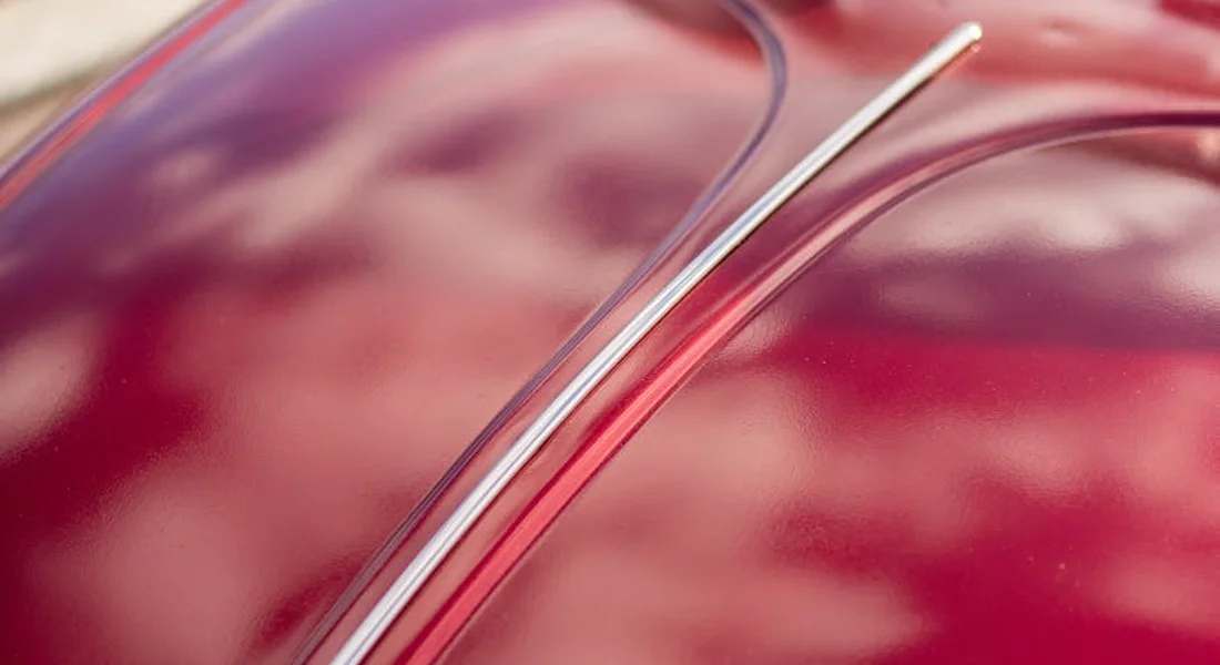 Close-up of a red car's paint with a scratch along the curved surface.