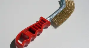 Red-handled wire brush used to lightly roughen and clean a car surface around chips or scratches for paint adhesion