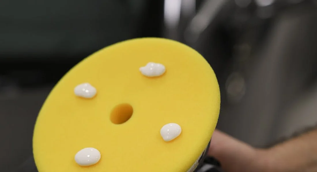 Close-up of a yellow foam polishing pad with white polish droplets