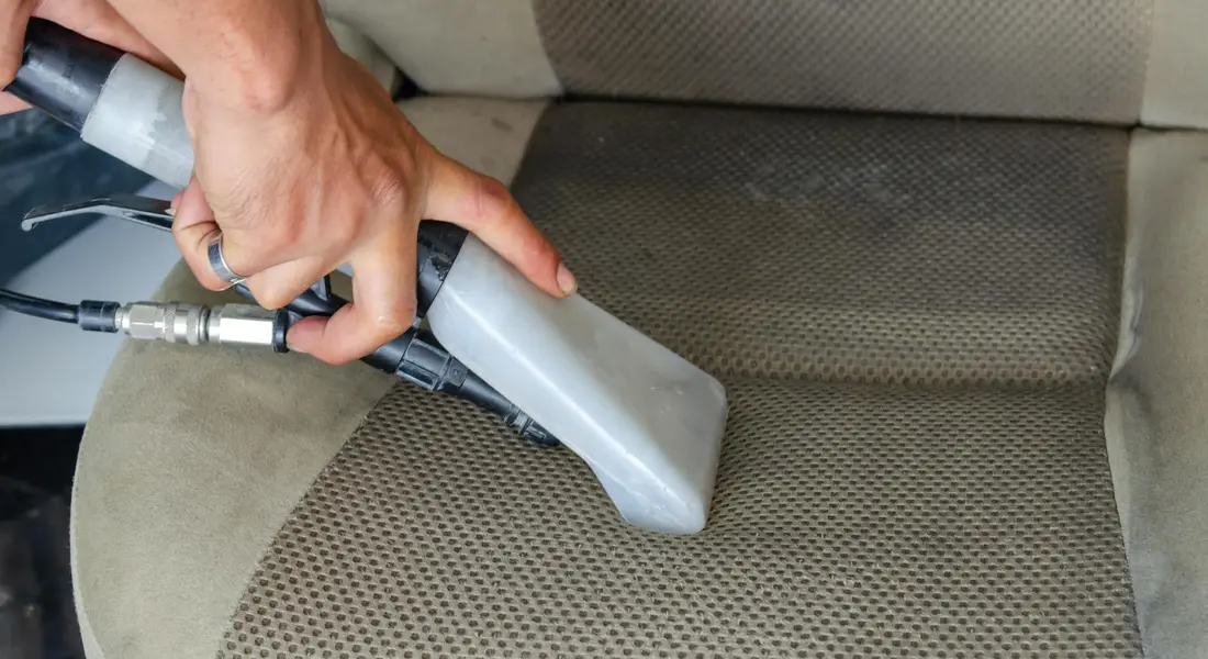 Handheld vacuum cleaner nozzle cleaning a car seat interior