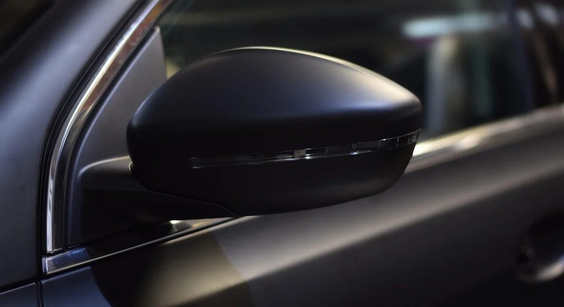 Close-up of a black car side mirror with a portion of the car window and body in the background