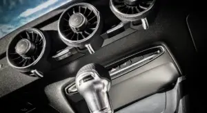 Close-up of car dashboard air vents with a small odor-removal tool inserted into the central vent.