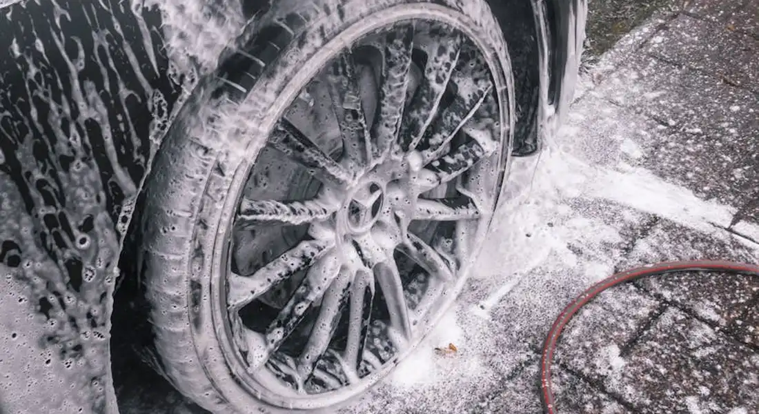 Close-up of a car wheel and tire covered in white soap suds during washing