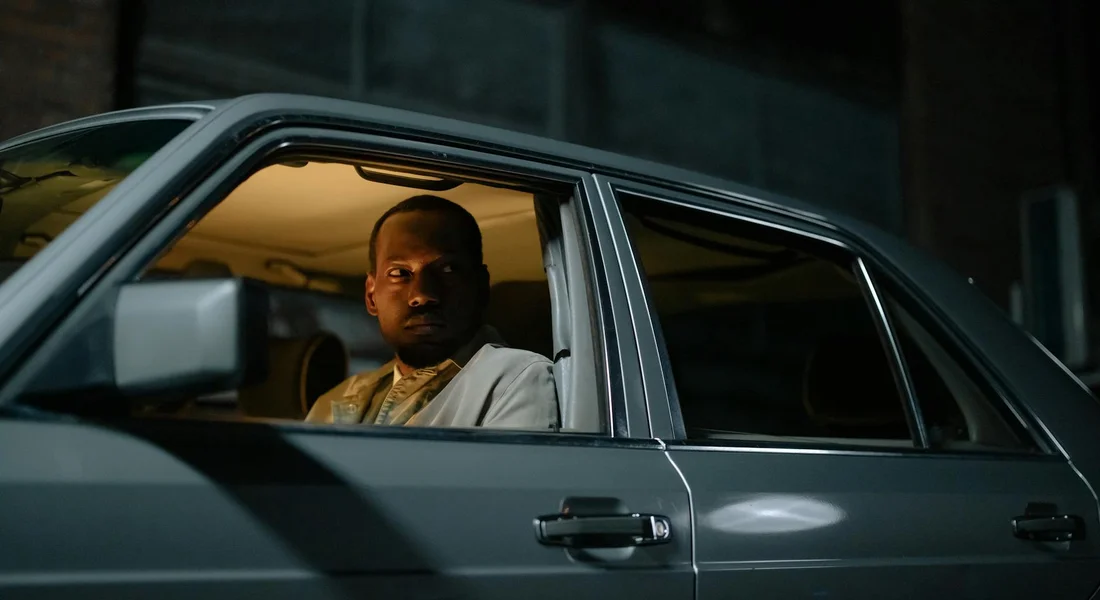 Person visible through the driver's window of a parked car, interior lighting showing the car window area.